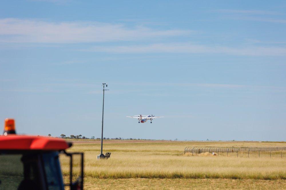 Aircraft approaching Longreach Airport runway over grassy airfield with clear blue sky in the background.