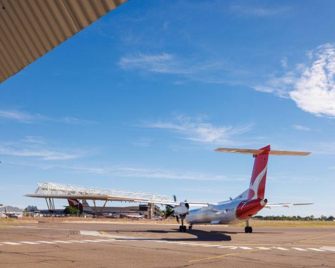 QantasLink aircraft parked on the apron at Longreach Airport with terminal building in the background under a clear blue sky.