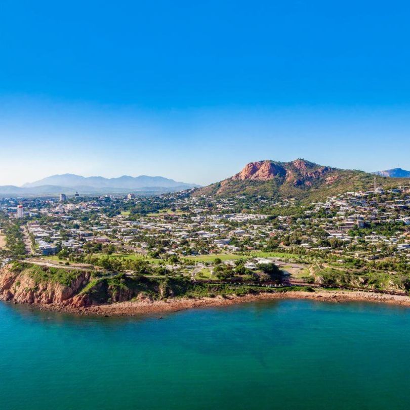  Aerial view of Townsville coastline with rocky shore, urban area, and Castle Hill in the background.