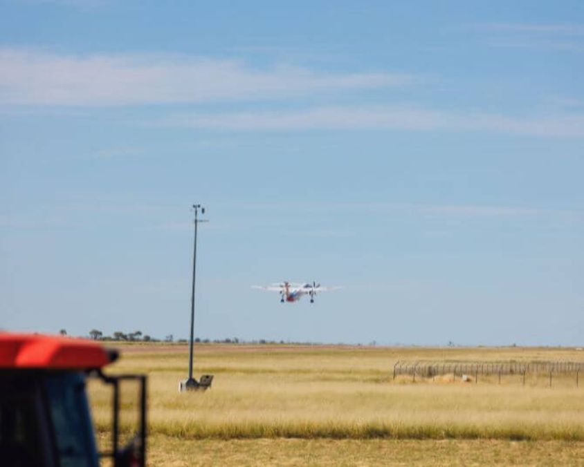 Aircraft approaching Longreach Airport runway over grassy airfield with clear blue sky in the background.